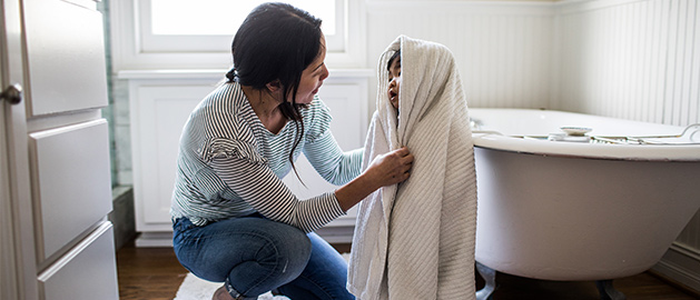 Mother wrapping towel around toddler in bathroom